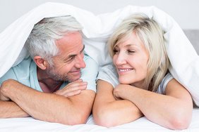 Glückliches mittelaltes Paar unter der Bettdecke